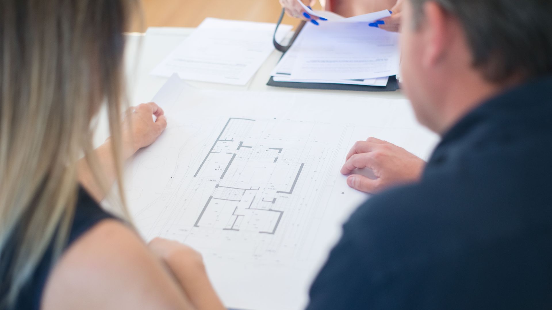 Architects discussing a detailed floor plan in an office setting, viewed from above.