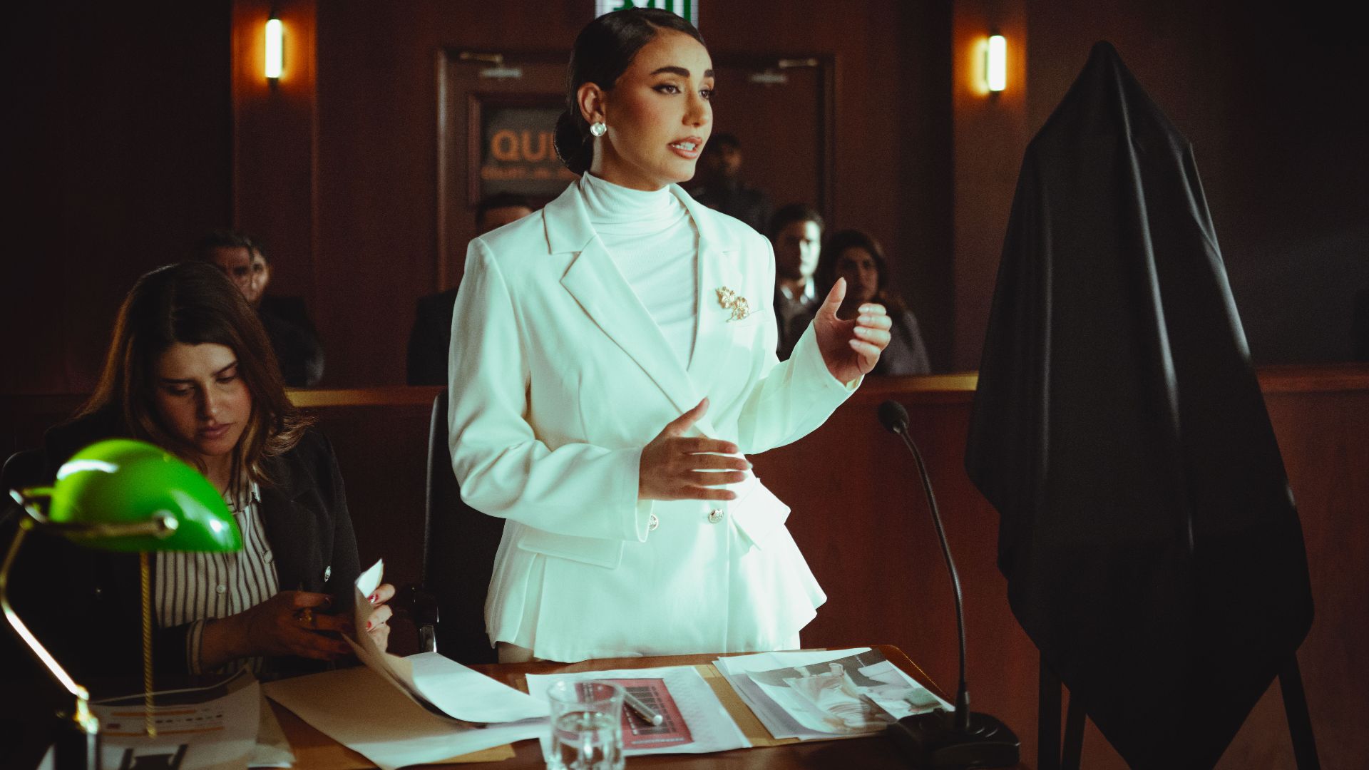 Confident woman in white suit presenting a case in an elegant courtroom setting.