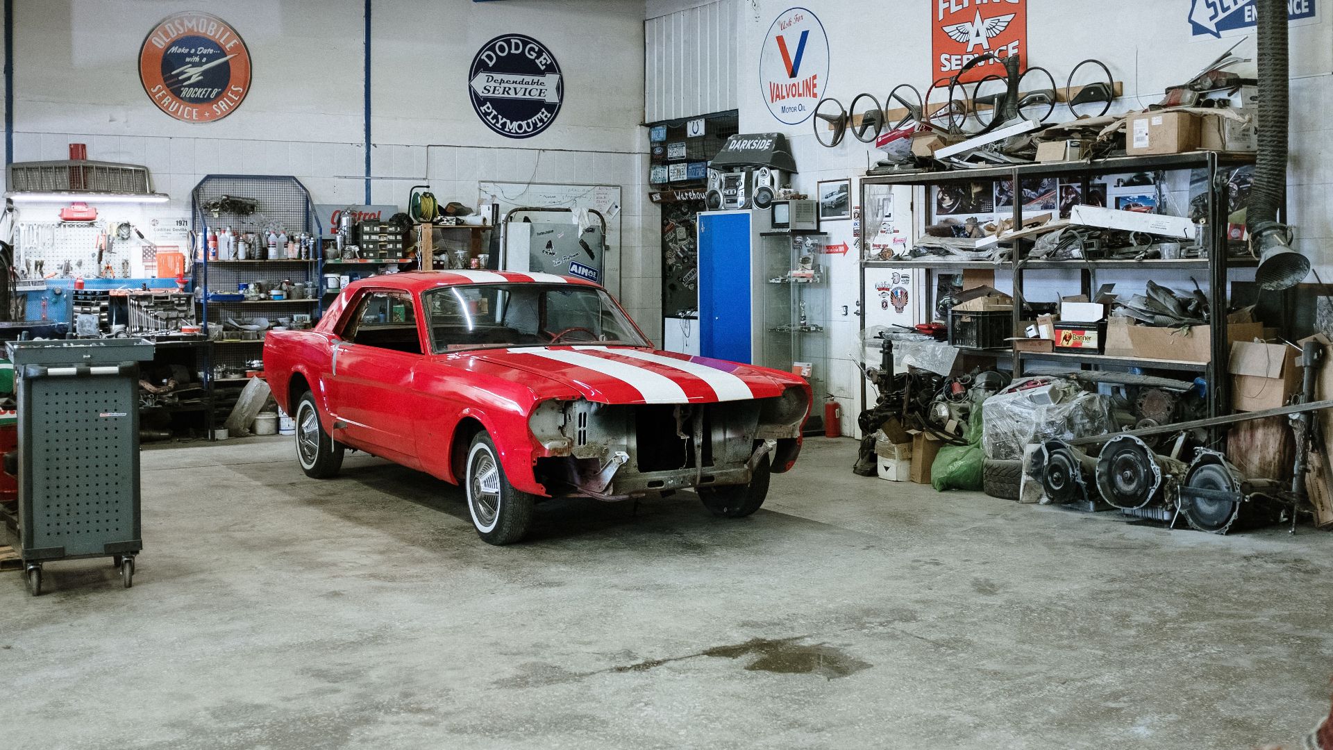 A vintage red car undergoing restoration in a well-equipped workshop with various tools and auto parts.