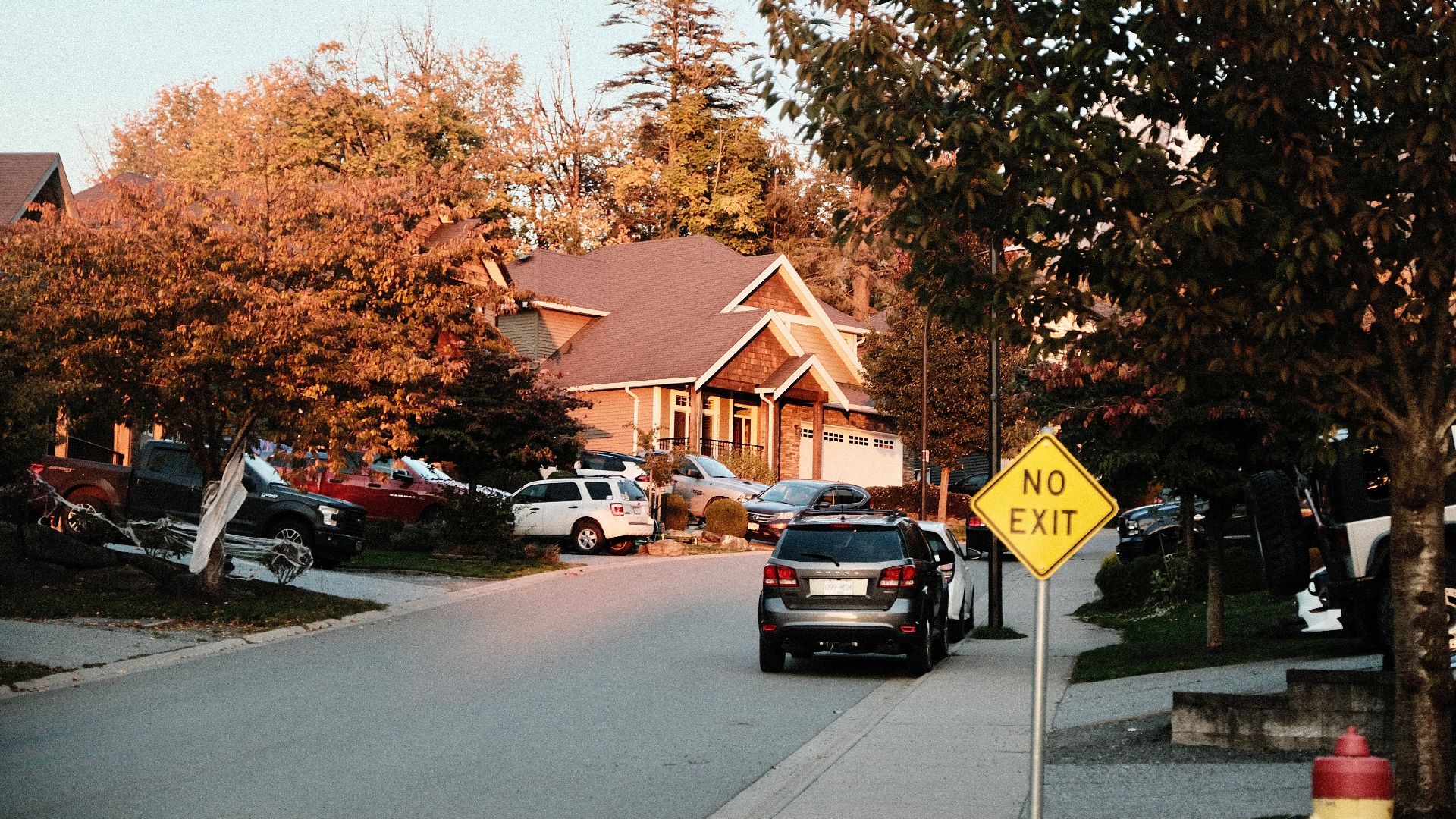 Charming suburban street scene with houses, cars, and a no exit sign in fall.