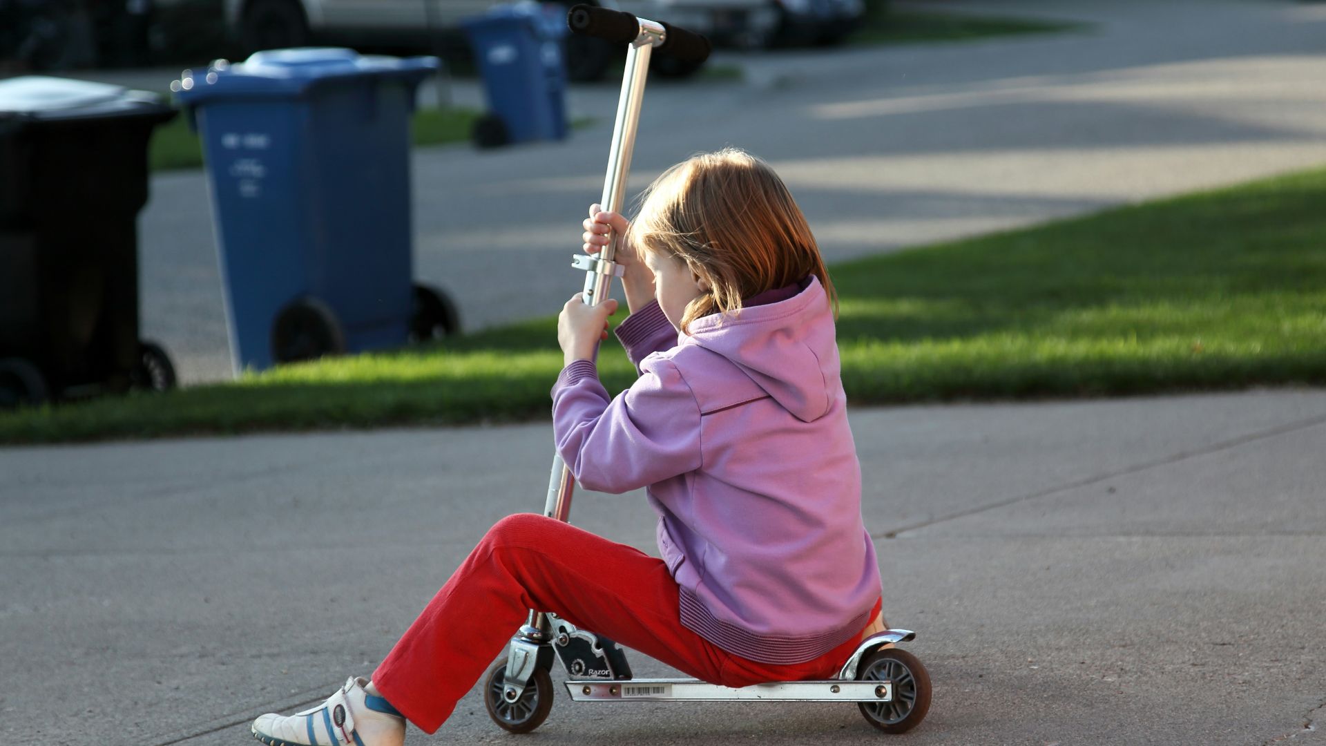 Young girl riding a scooter on a paved driveway.