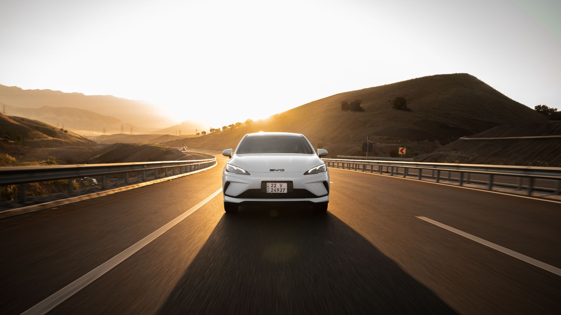 Electric car driving on a scenic highway at sunset, highlighting modern automotive design and sustainable travel.