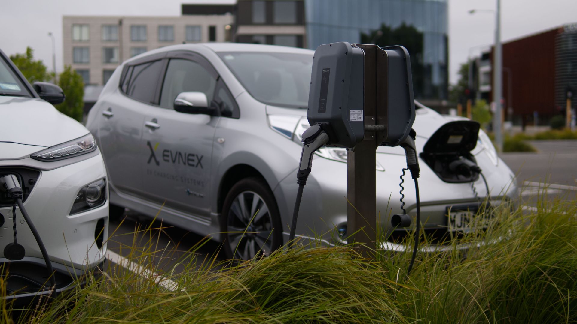 Electric vehicles at a charging station in Christchurch parking lot with modern architecture.