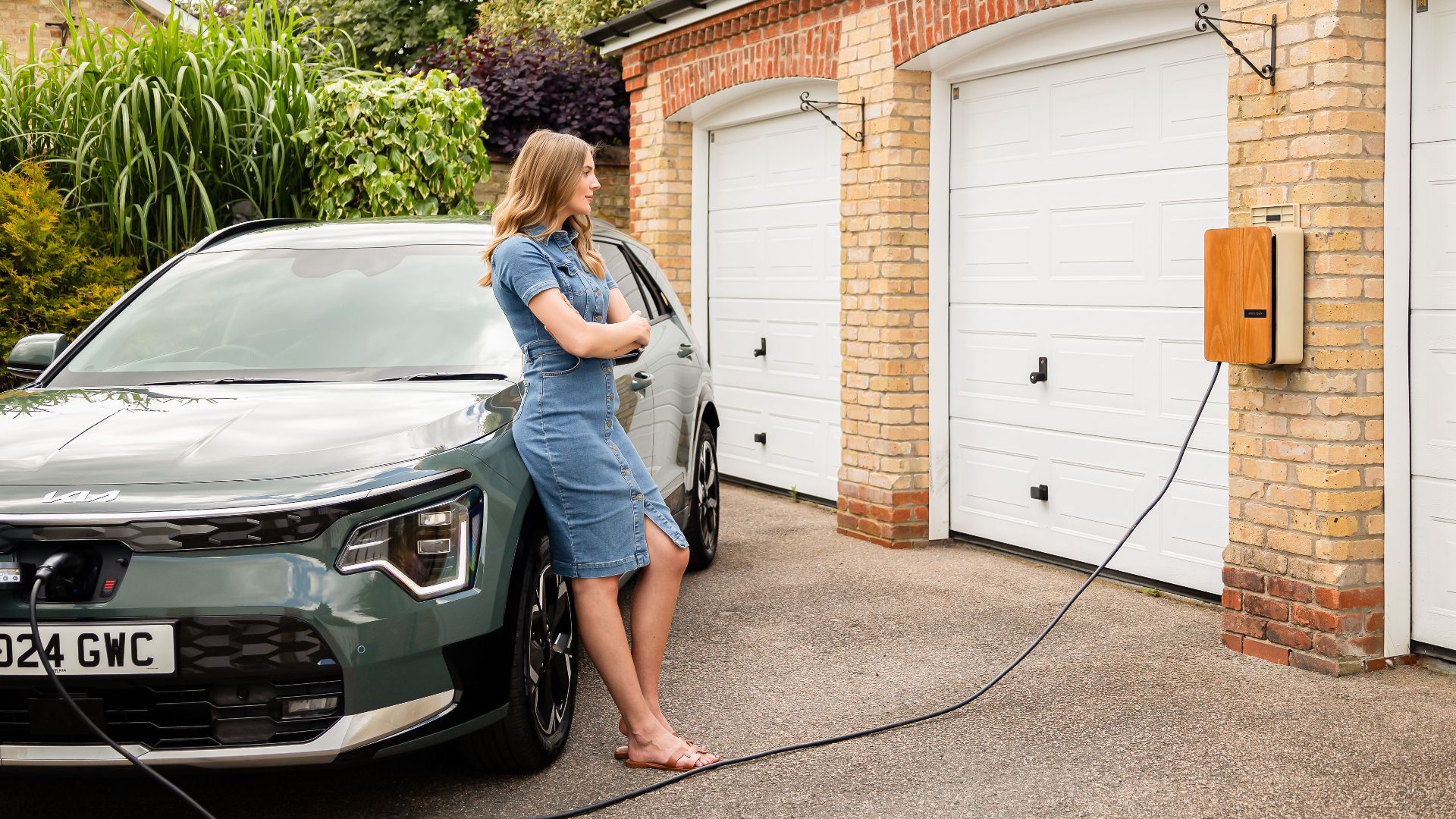 Woman charging electric vehicle at home with a modern wall-mounted charging station.