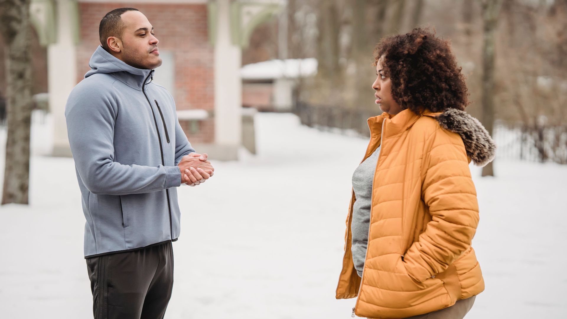 Side view of plump African American and black man in sportswear looking at each other while standing on snowy ground during workout