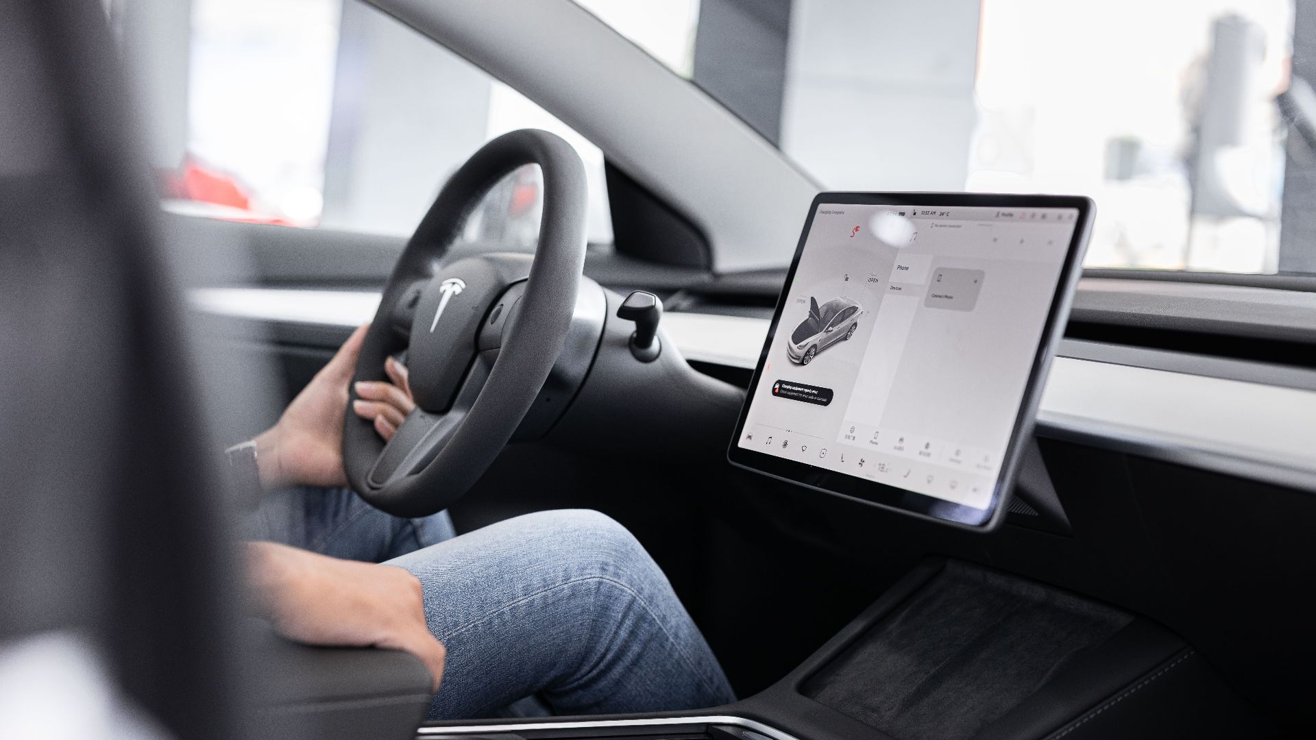 Interior of an electric car showing steering wheel and large touchscreen display, indicating modern technology.