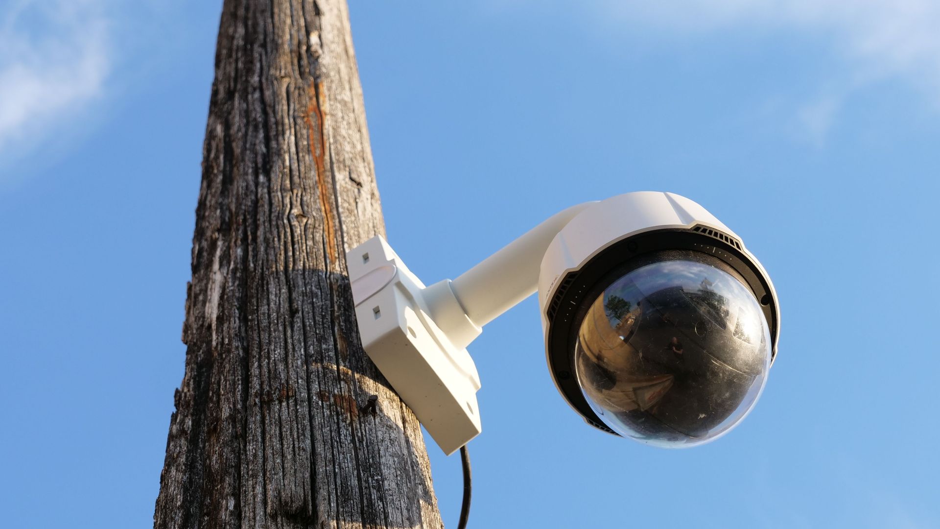 A security camera mounted on a wooden pole against a clear blue sky, highlighting urban surveillance.