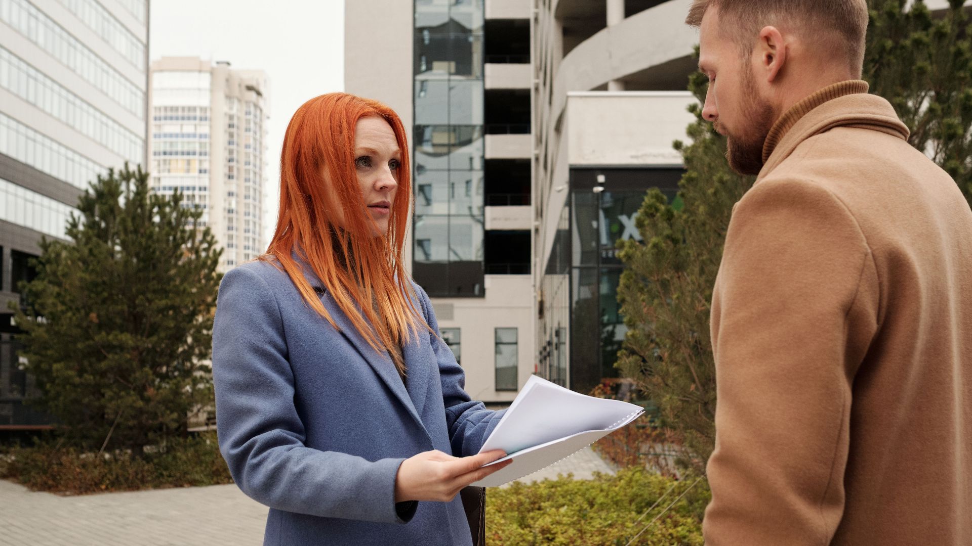 Man and woman in corporate attire engaging in conversation outside urban office complex.