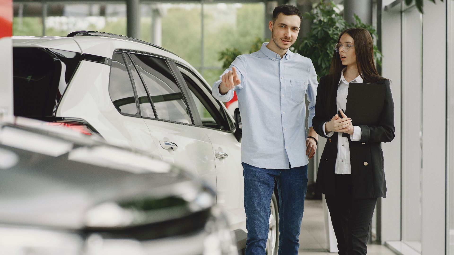 Customer and salesperson discussing a vehicle inside a modern car dealership showroom.