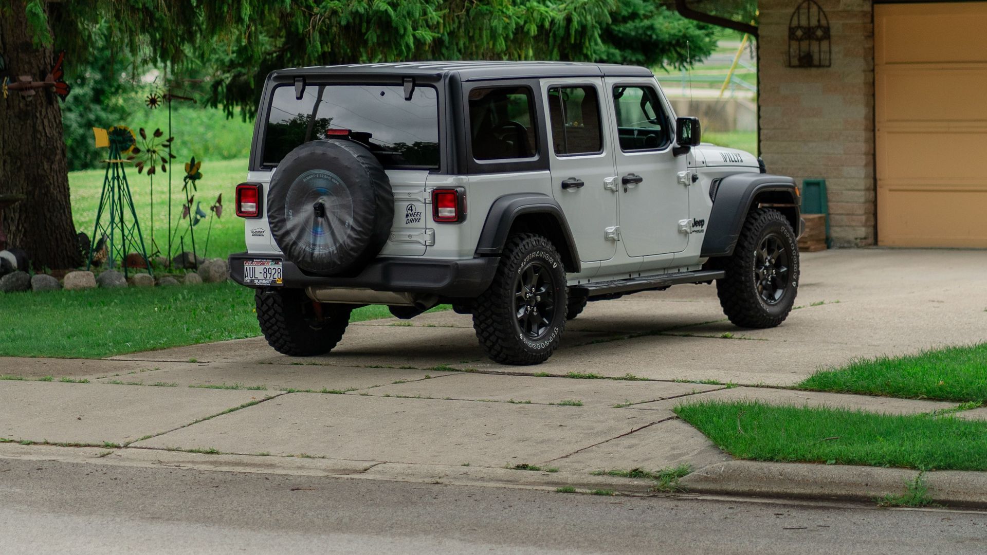 A silver SUV is parked in a suburban driveway surrounded by green trees and grass.