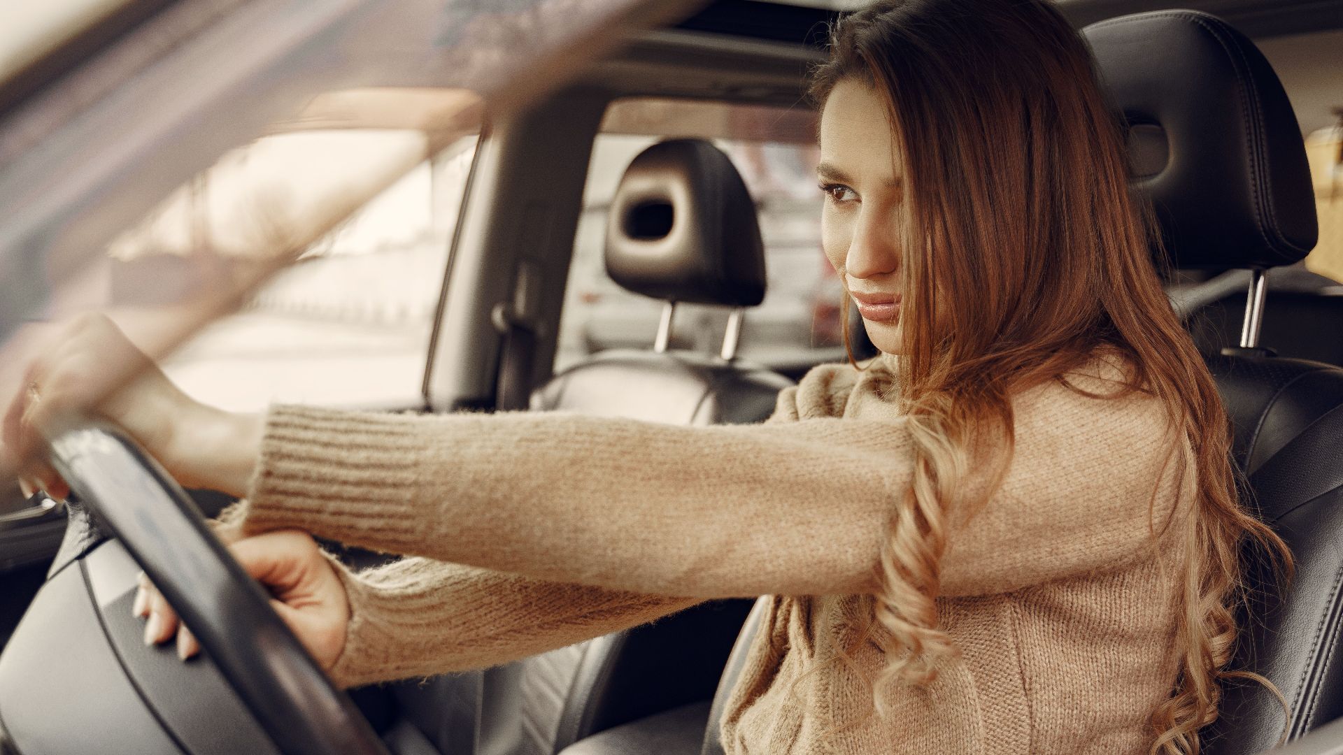 Side view of concentrated contemporary female driver in casual clothes going along street road alone by car with leather interior