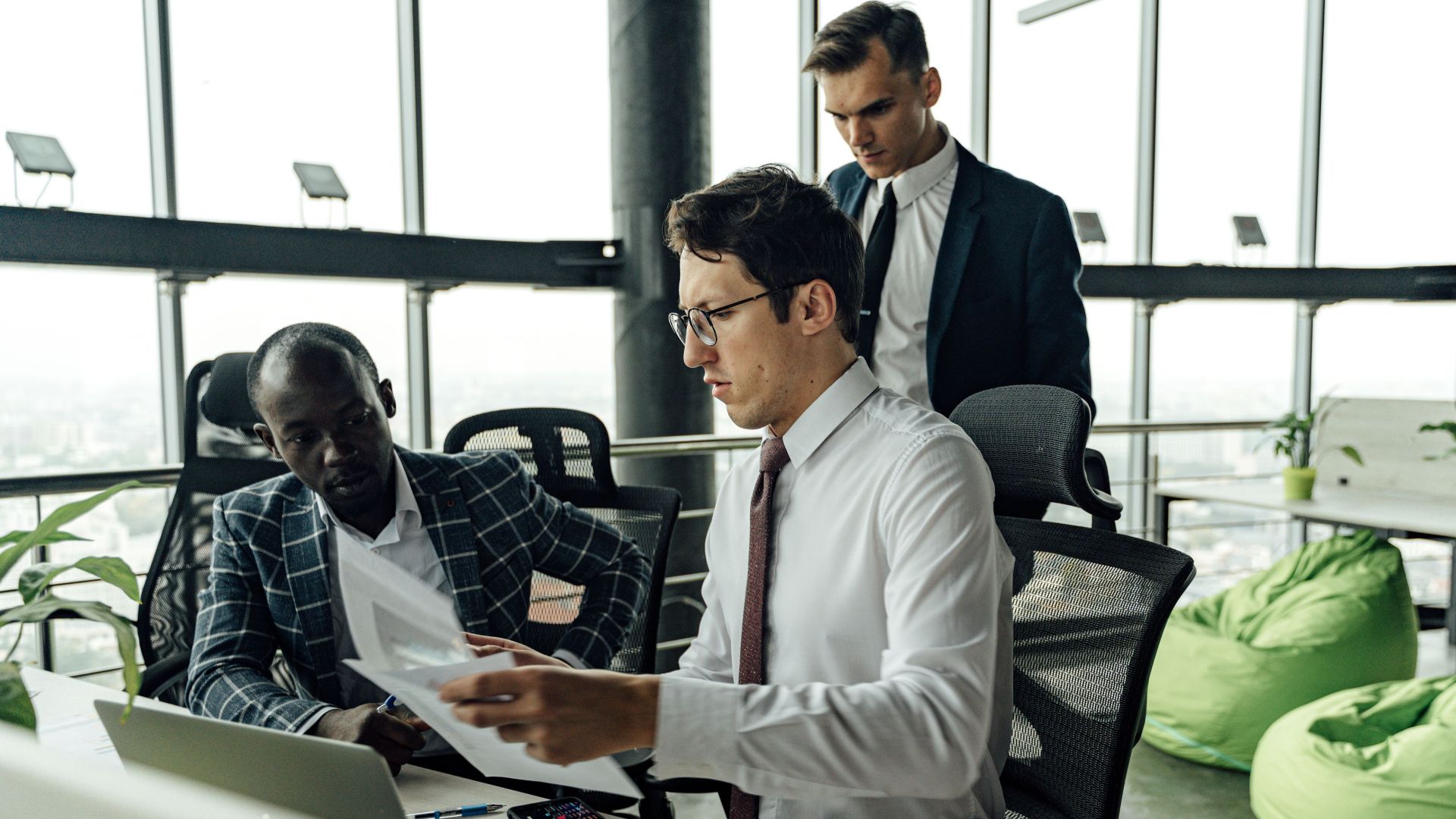 Professionals engaging in teamwork and discussion in a contemporary office setting with large windows.