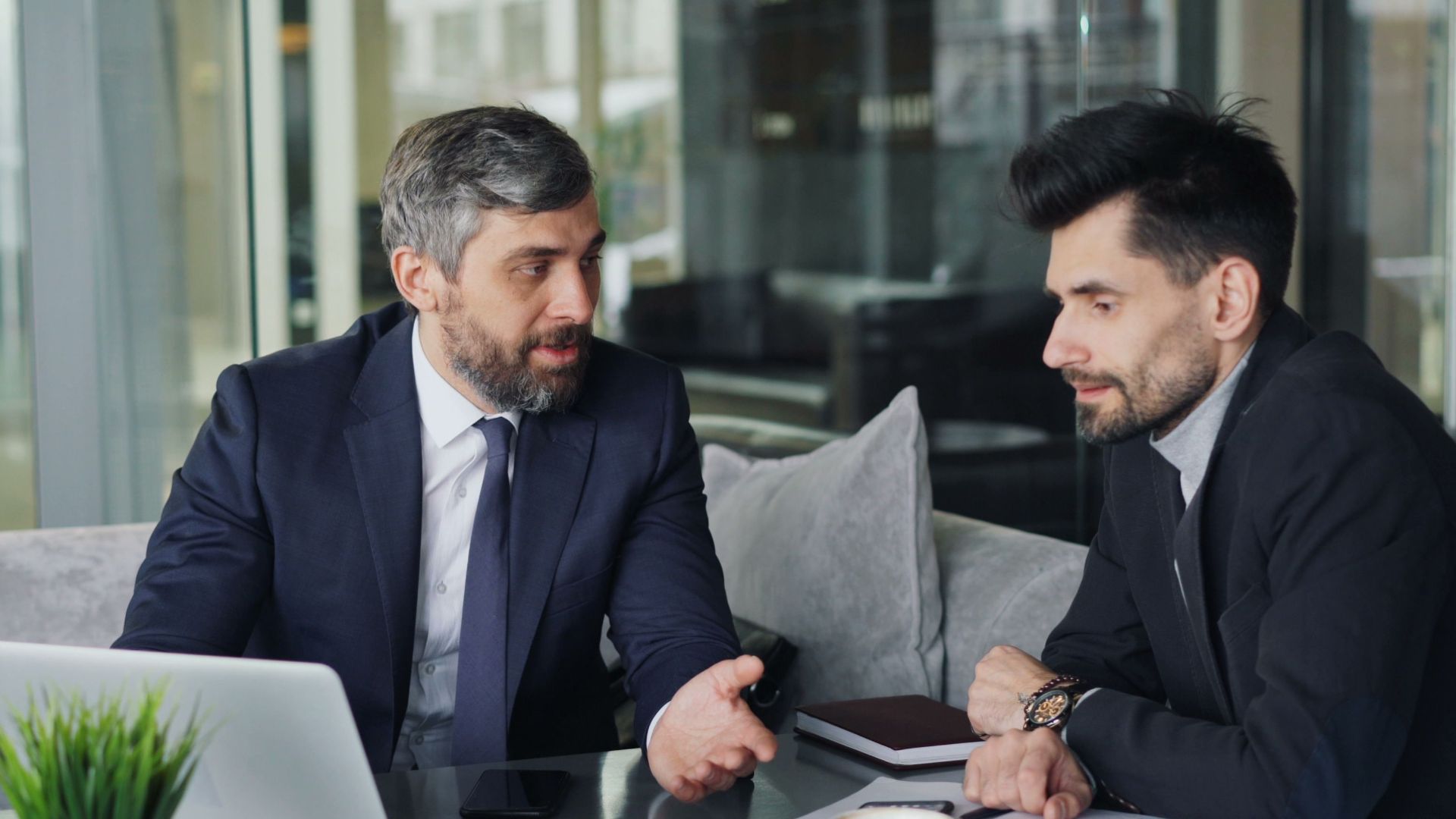 Two businessmen in a café having a professional discussion with coffee and a laptop.