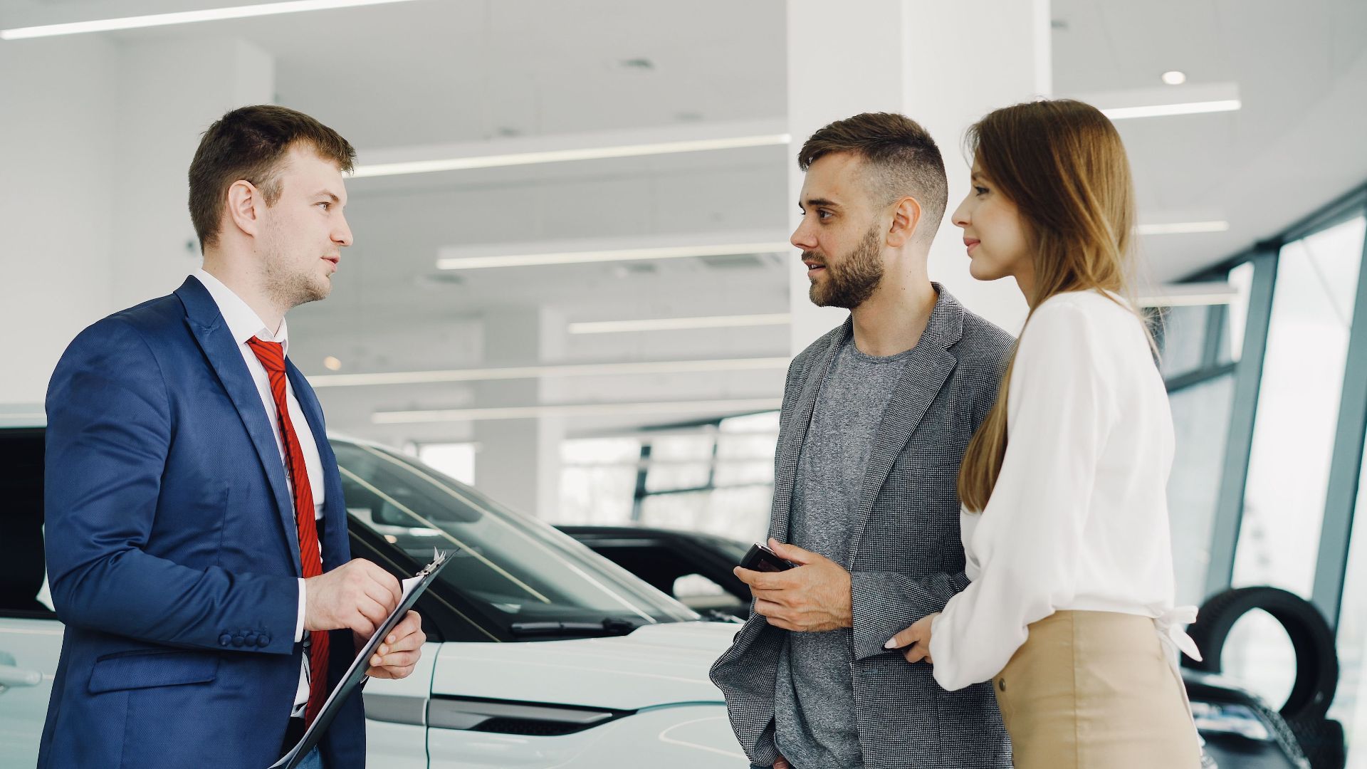 Car salesman assisting a couple in a modern showroom with a luxury car.