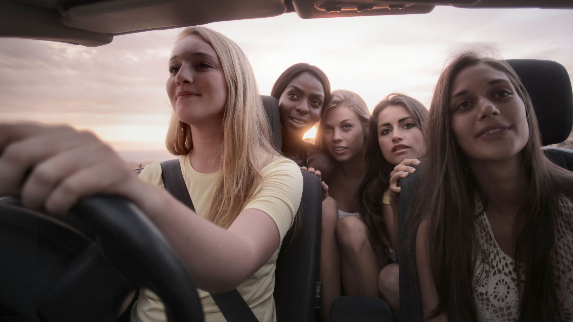 Five women sharing a joyful road trip at sunset, symbolizing friendship and adventure.