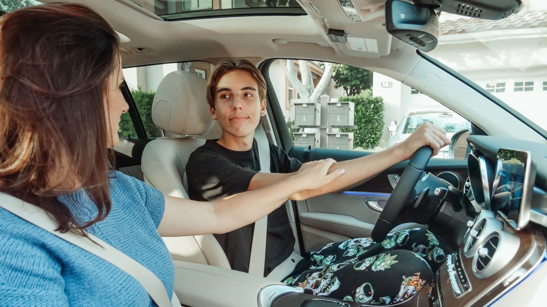 A mother supports her teenage son as he learns to drive in a car