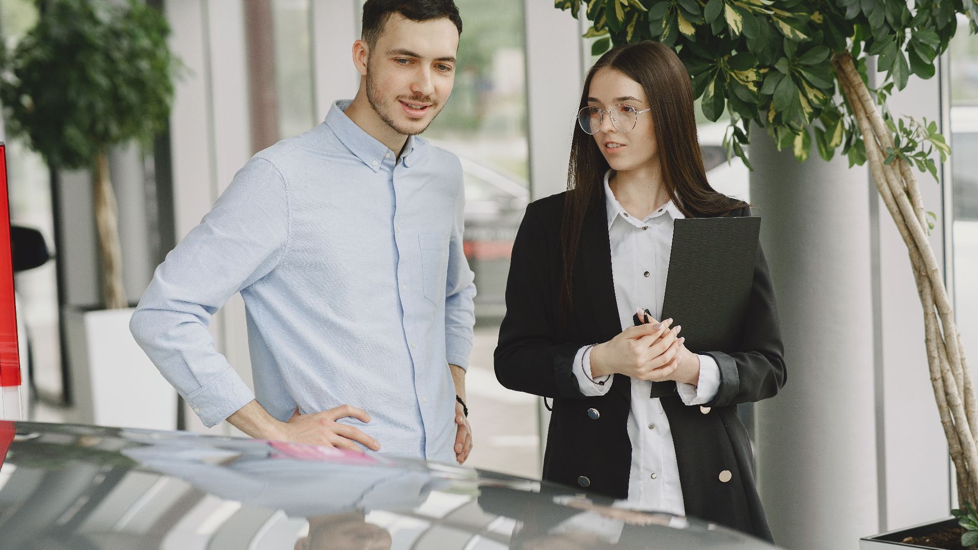 Two professionals discussing business in a modern car showroom with plants around.