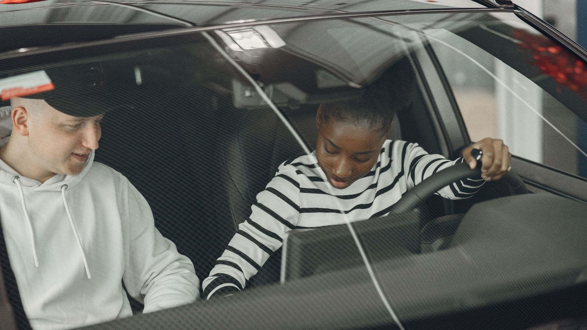 Black woman and caucasian man sitting inside a vehicle, discussing driving.