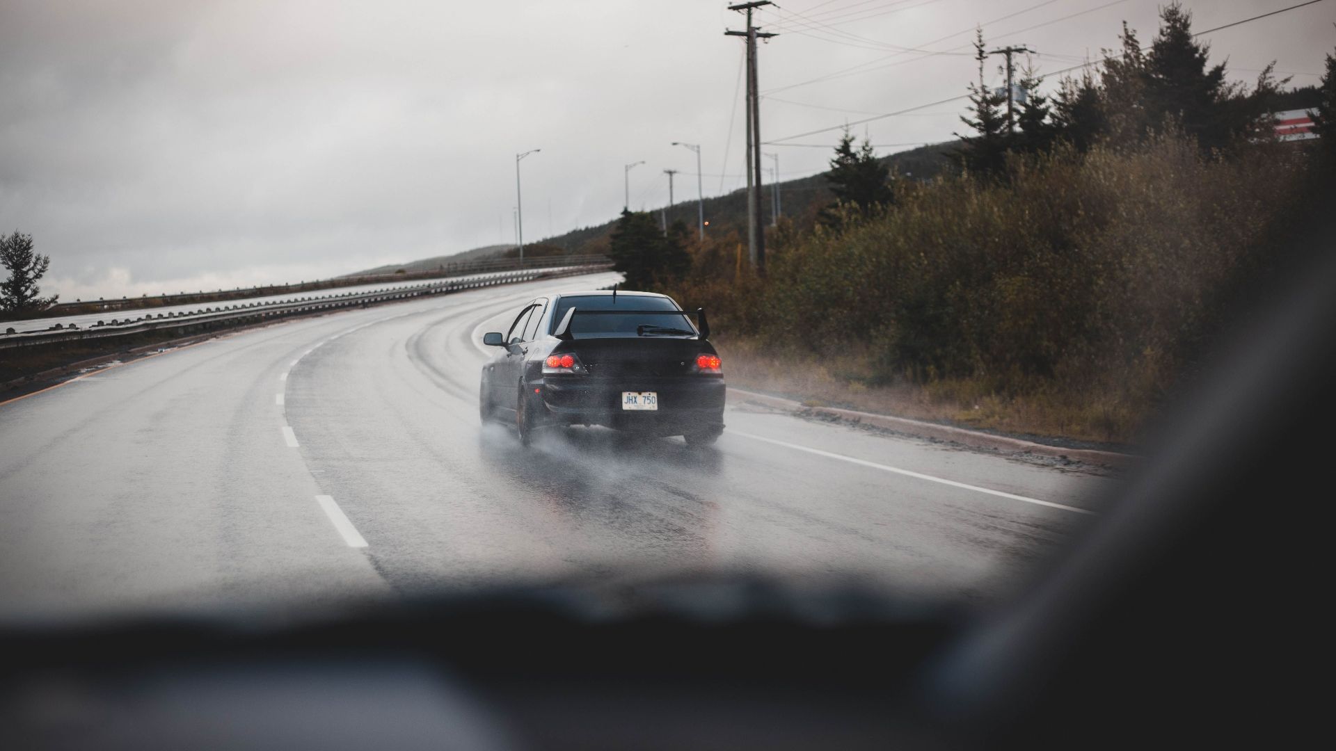 A black car drives on a rainy highway, showcasing speed and transportation.