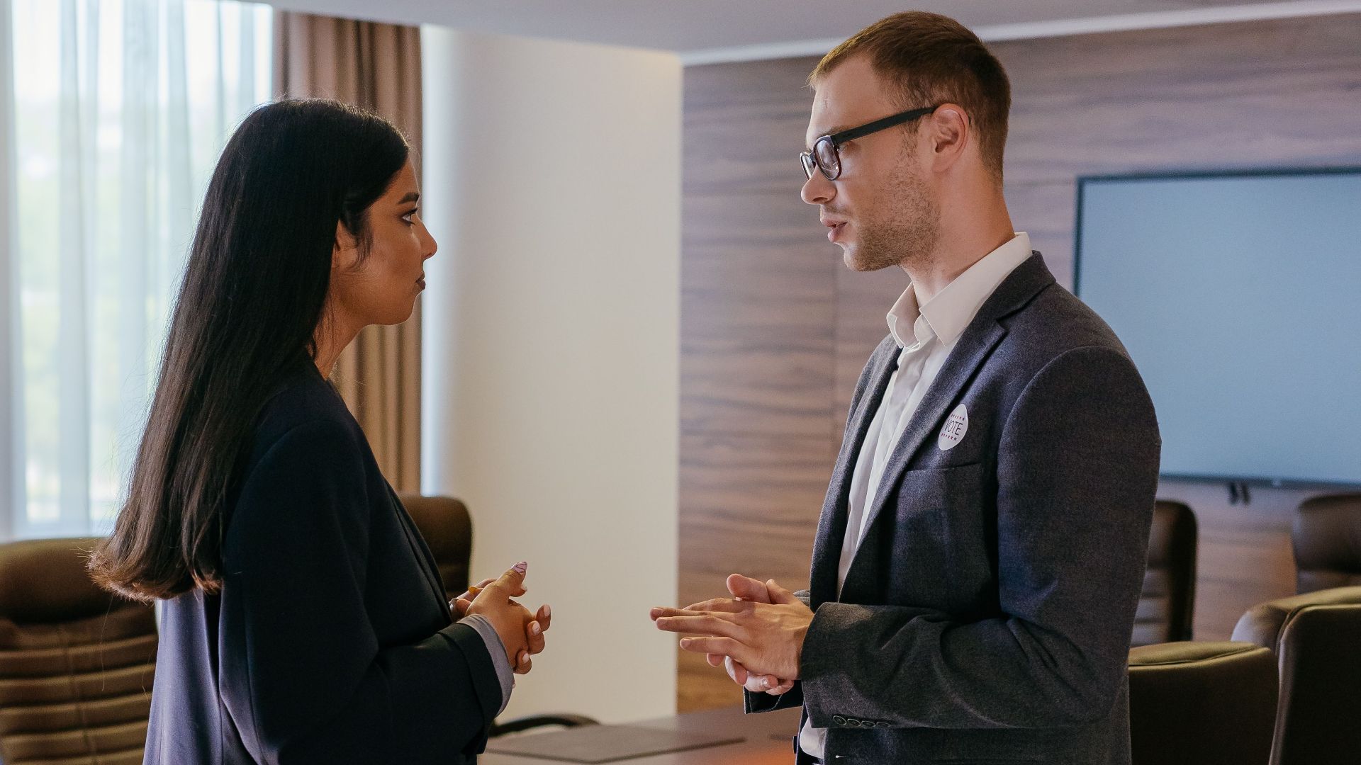 Two professionals engaged in discussion inside a modern conference room setting.