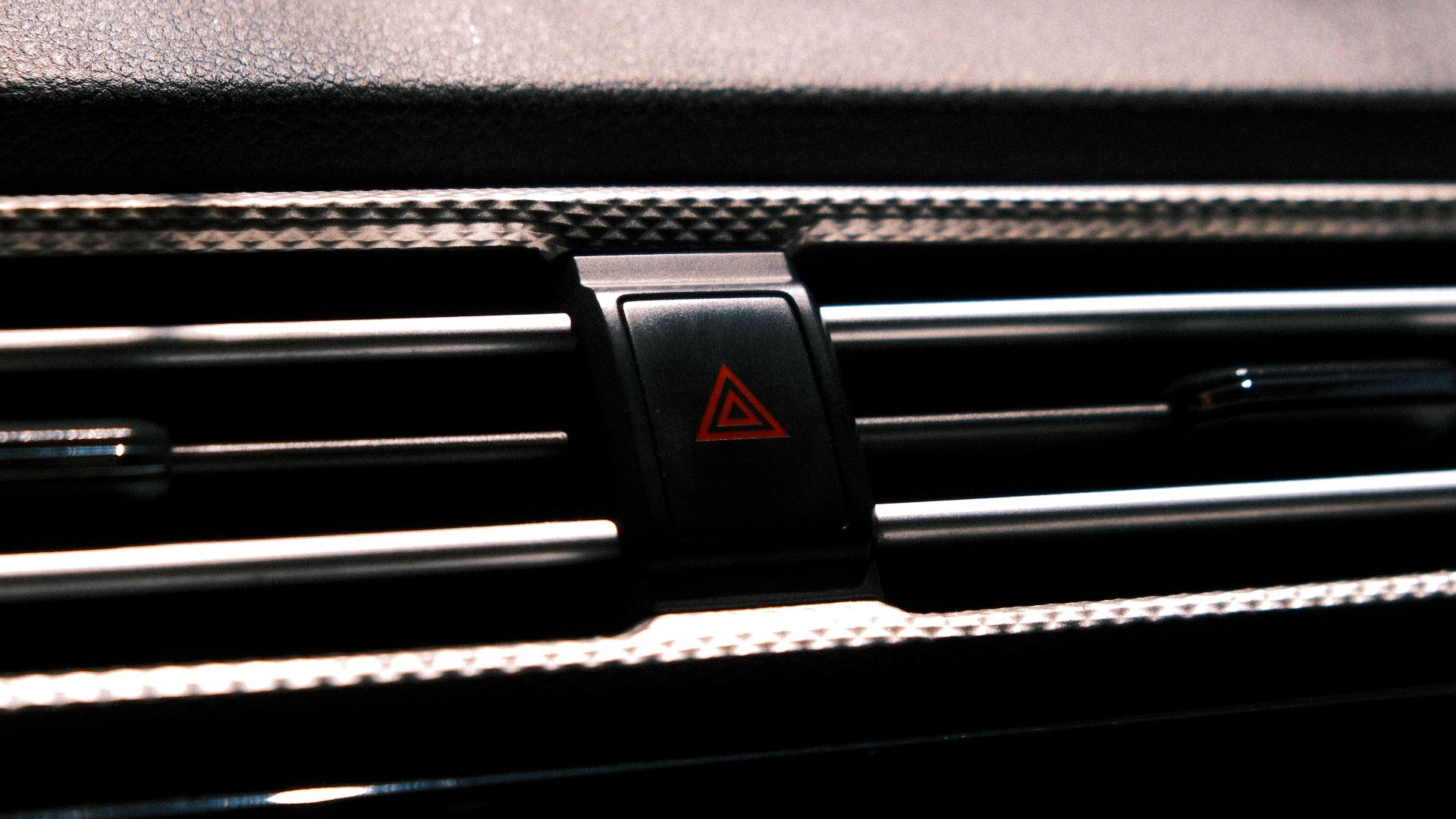 Close-up image of a car hazard light button on a dark dashboard.