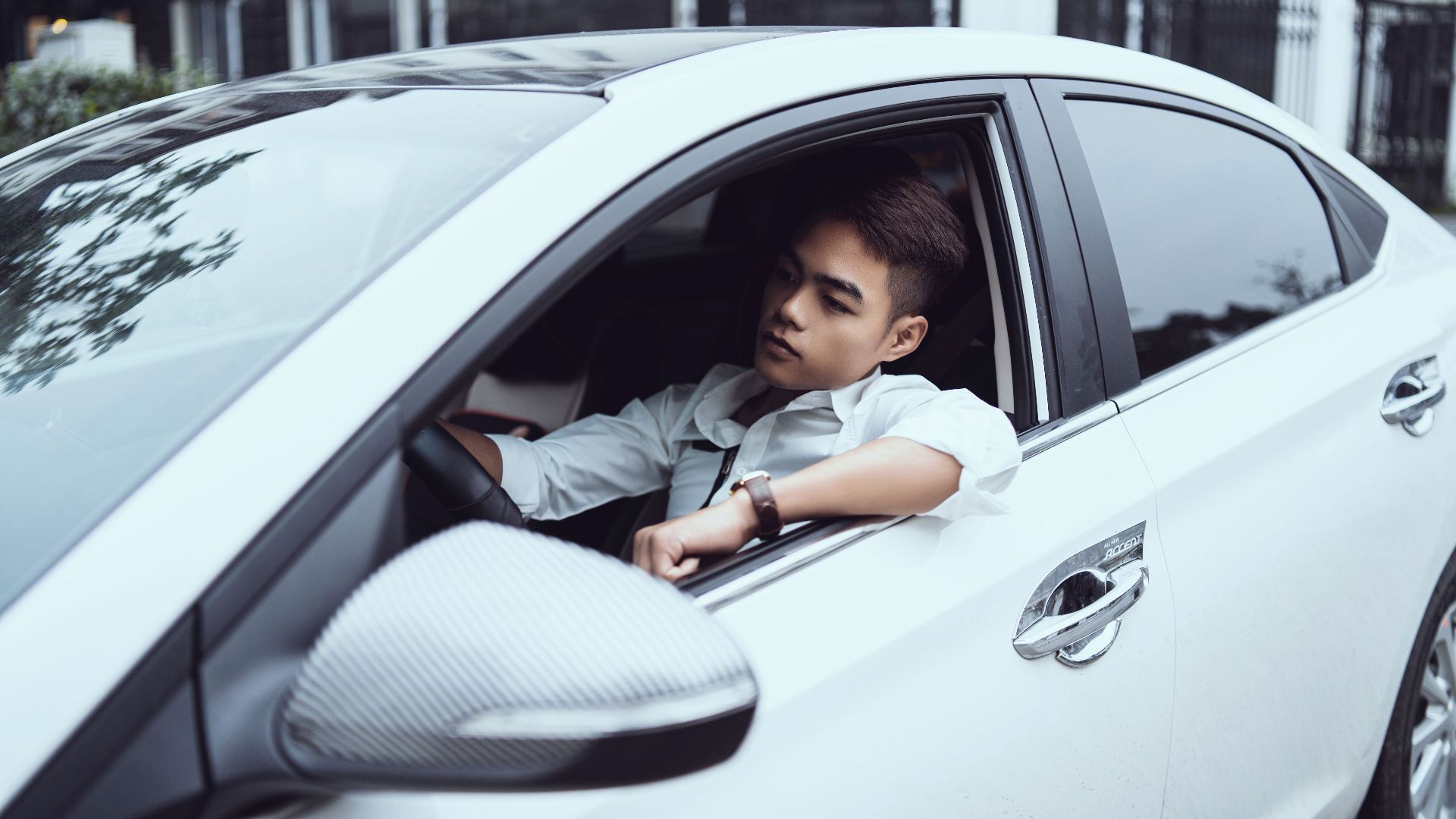 Self assured young ethnic male in white shirt driving modern car on city street in daytime