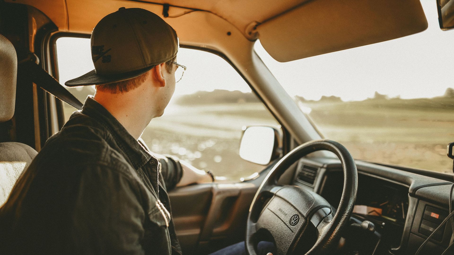 A man enjoys a relaxed drive through the countryside on a sunny day, looking out onto the scenery.