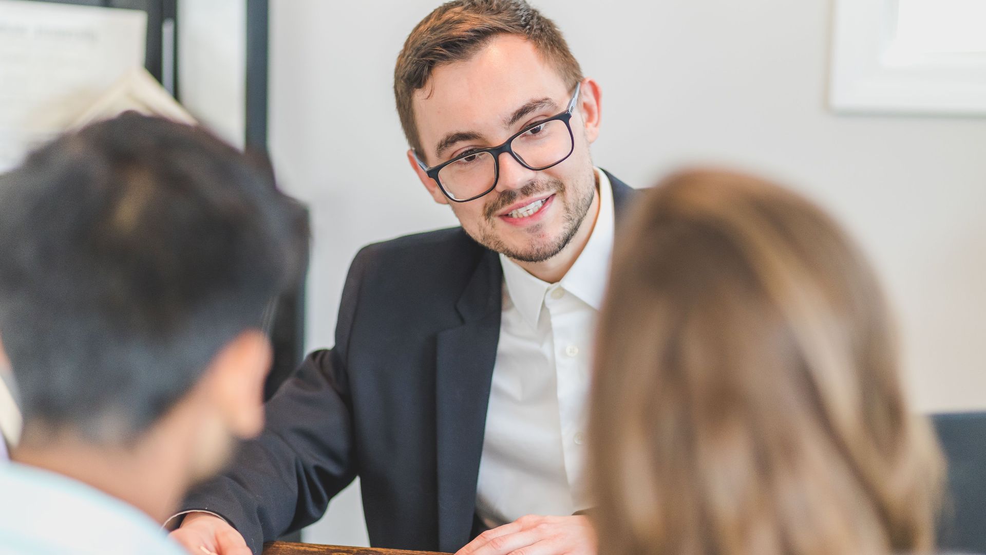 Smiling businessman in a suit and eyeglasses during a team discussion.