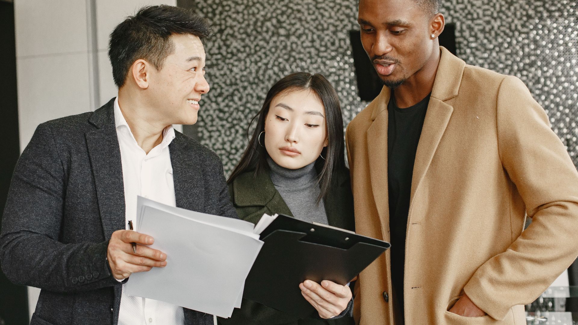 Three diverse professionals discussing a document indoors, showcasing teamwork and collaboration.