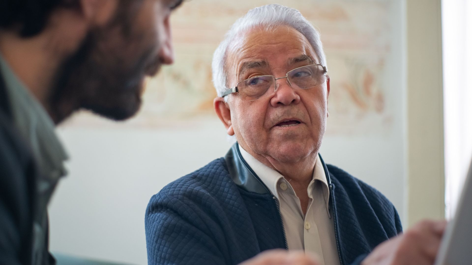 Elderly man with eyeglasses in a thoughtful discussion in Portugal indoors.