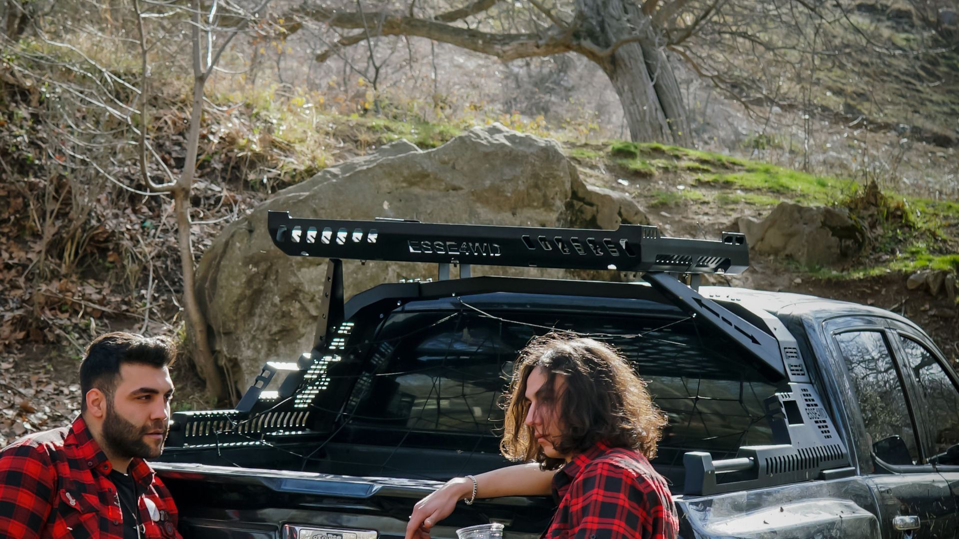 Two men enjoying a break with a pick-up truck in a forest setting, wearing matching plaid shirts.