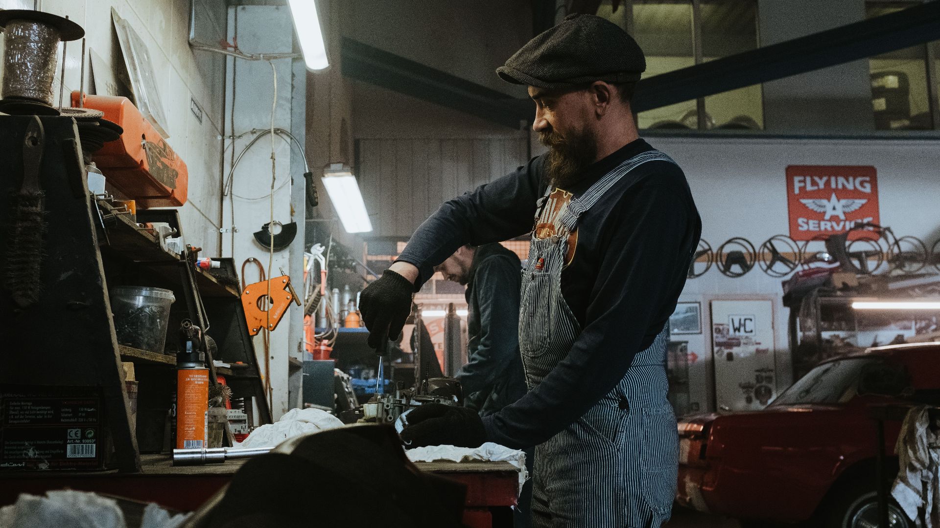 Mechanic performing repairs in a vintage garage setting, using tools and machinery.
