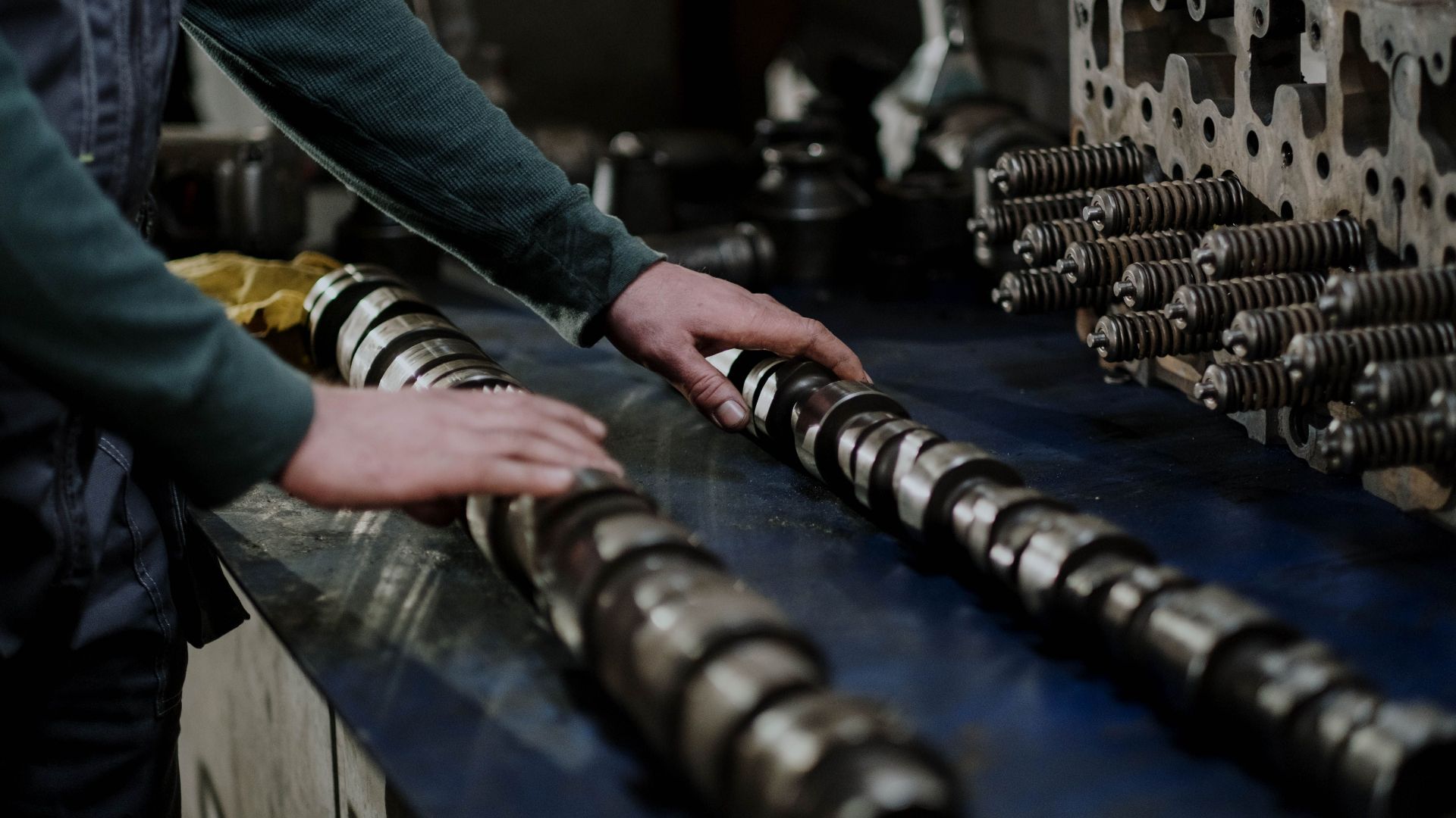 Worker handling camshafts and cylinder head in a mechanic workshop.