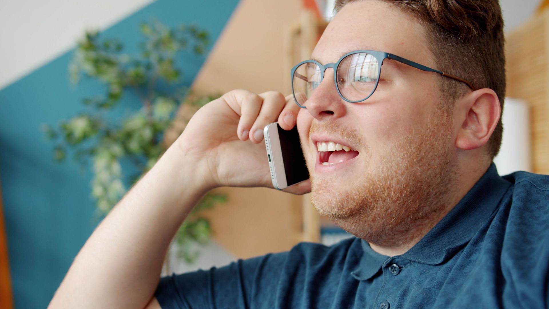 Happy adult man with glasses having a phone conversation inside a bright room.