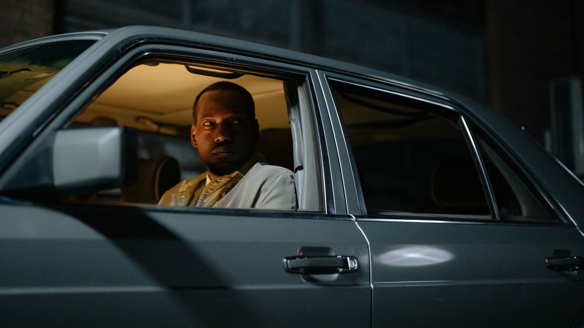 A man looks vigilantly from a car window during nighttime, showcasing alertness.