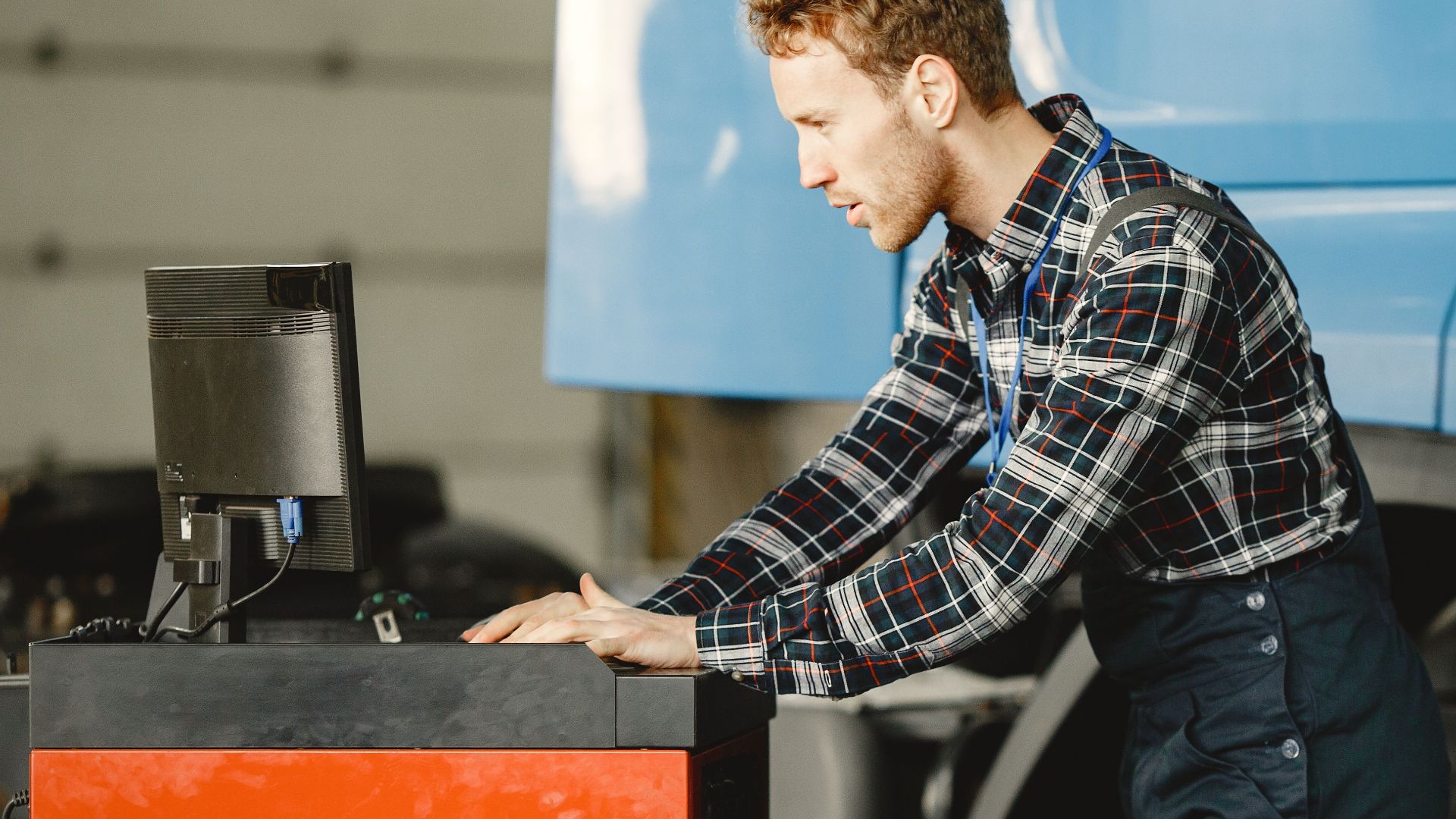 A mechanic focuses on a computer to diagnose and repair a large truck in a workshop.