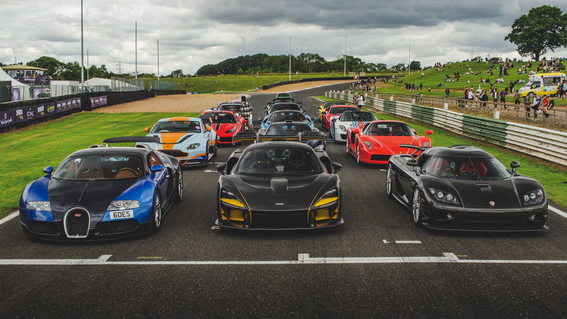A lineup of luxury sports cars ready for a racing event at an outdoor track.