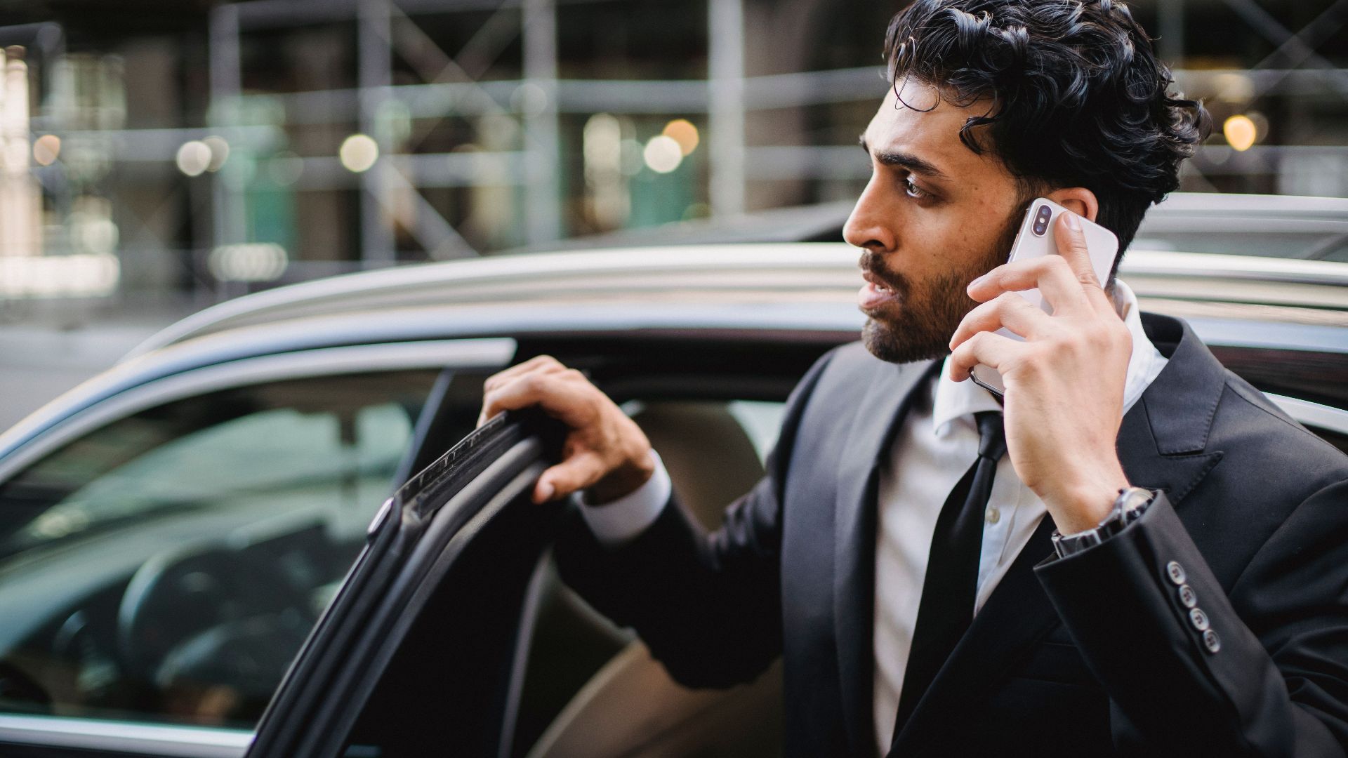 A businessman in a suit talking on his smartphone while exiting a vehicle.