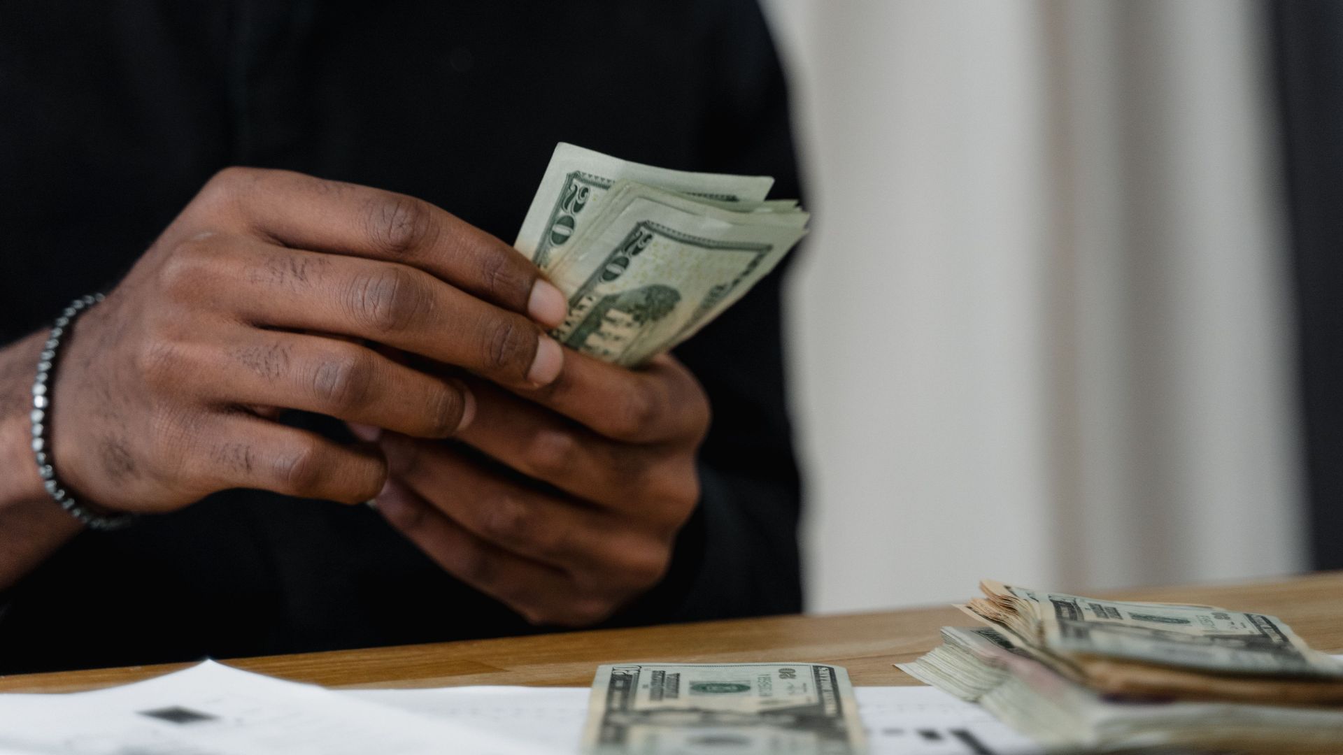Adult counting dollar bills at a desk, focused on money management and finance.