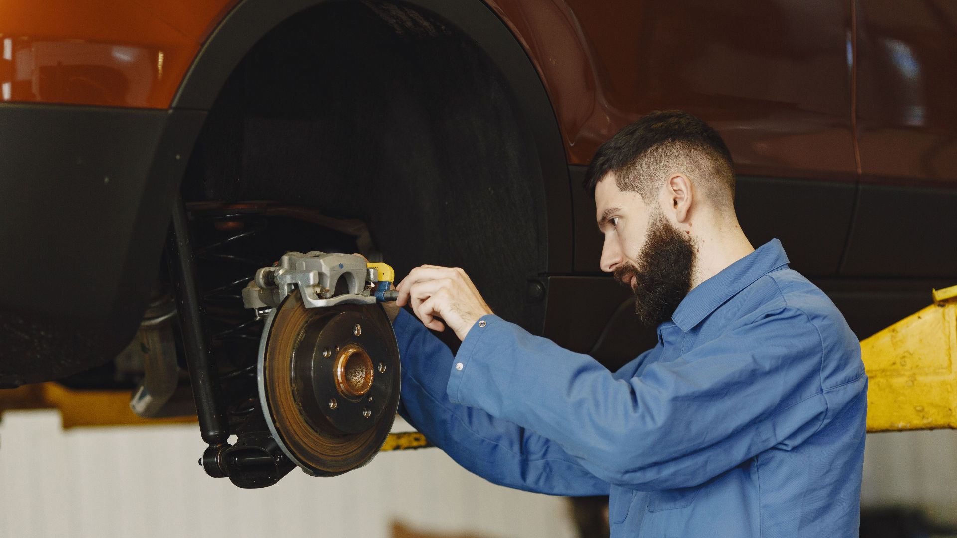 Mechanic in blue uniform performing brake repair on car in modern garage.