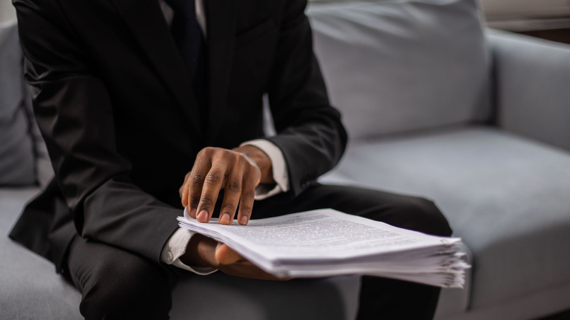 Close-up of a businessman in a suit reviewing documents while seated on a sofa indoors.