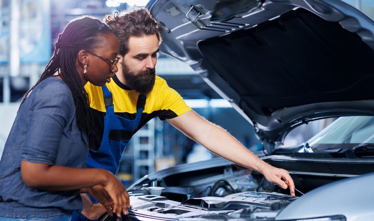 Mechanic at auto repair shop conducts annual vehicle checkup, informing customer about needed motor replacement. Garage employee talking with customer after finishing car inspection