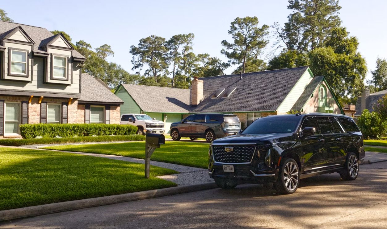 Black suv parked on a sunny suburban street with houses.