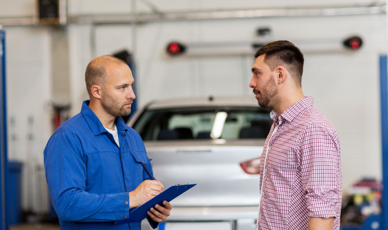 auto service, repair, maintenance and people concept - mechanic with clipboard talking to man or owner at car shop