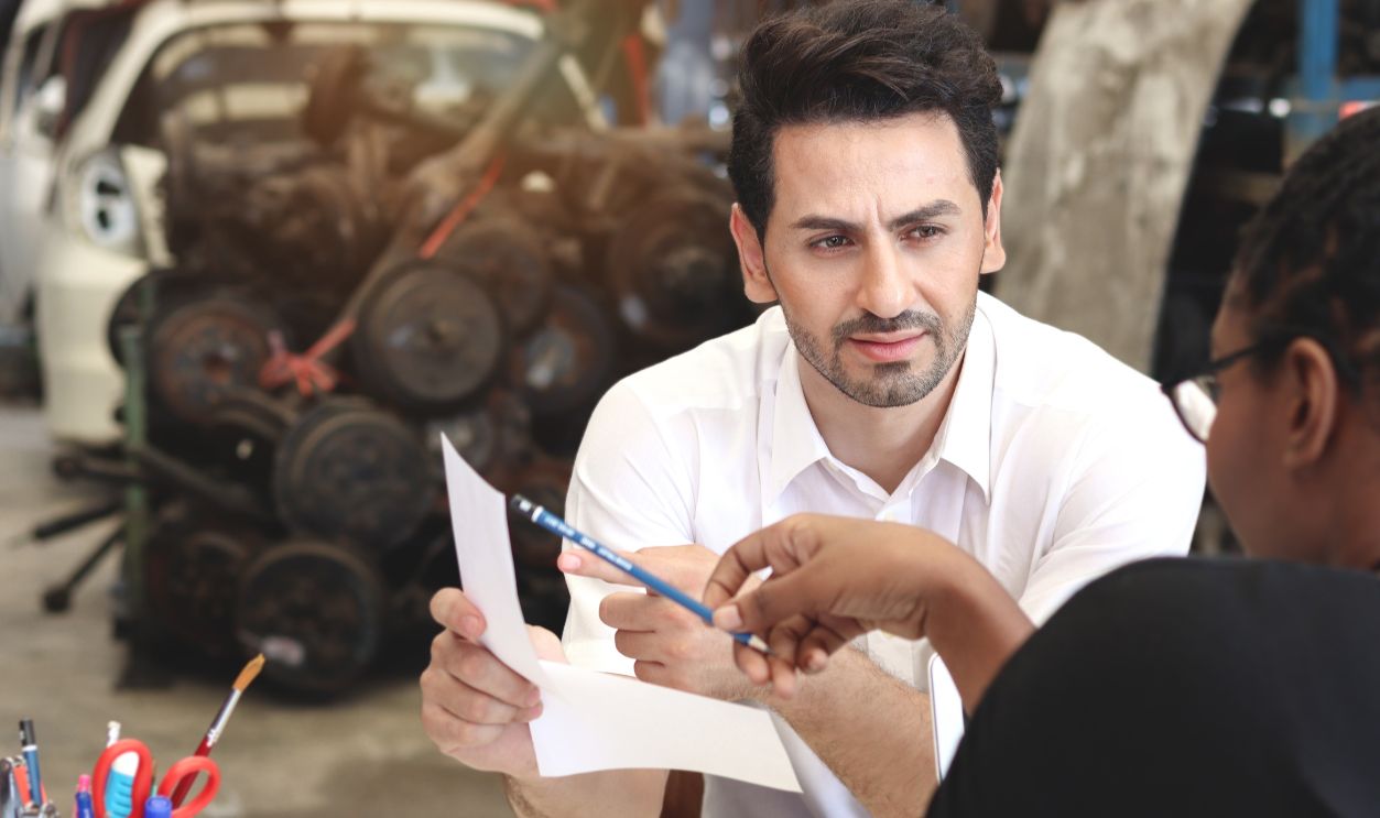 Unhappy man feels confused by employee description the prices of services and products in auto spare parts store warehouse with secondhand engine parts. Buyer disagrees with the price calculation.