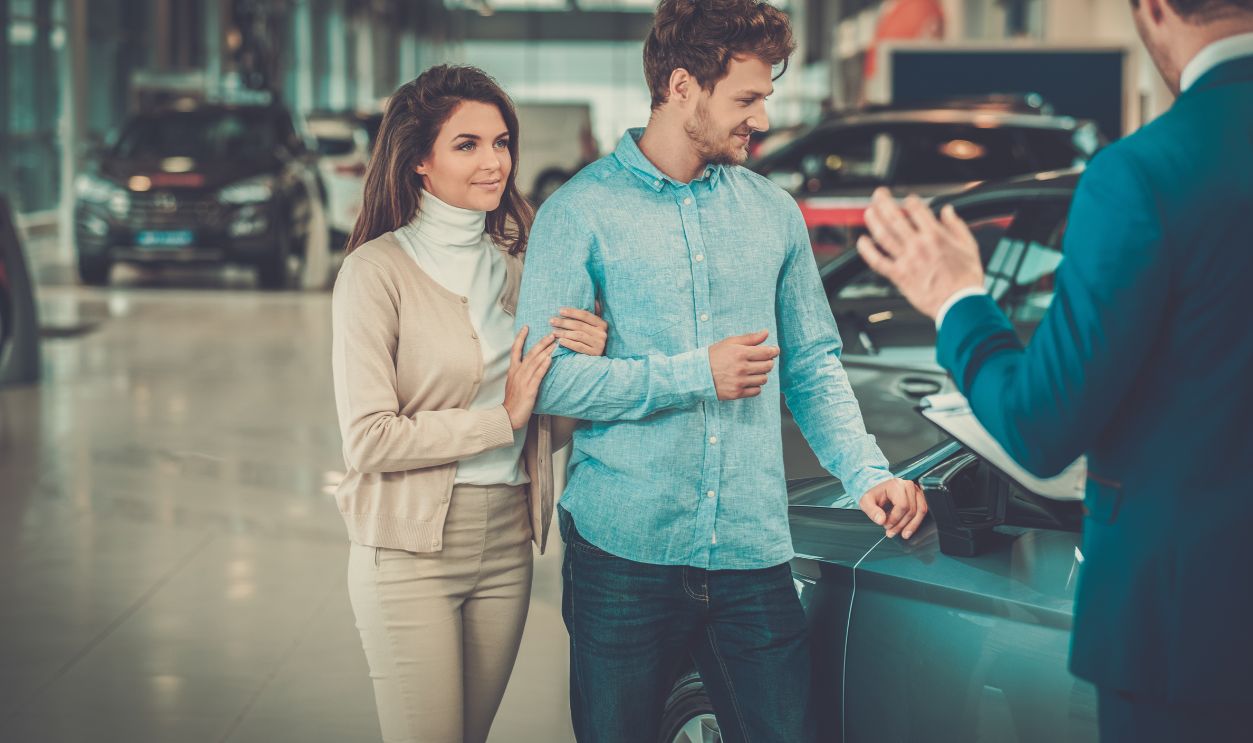 Salesman talking to a young couple at the dealership showroom.