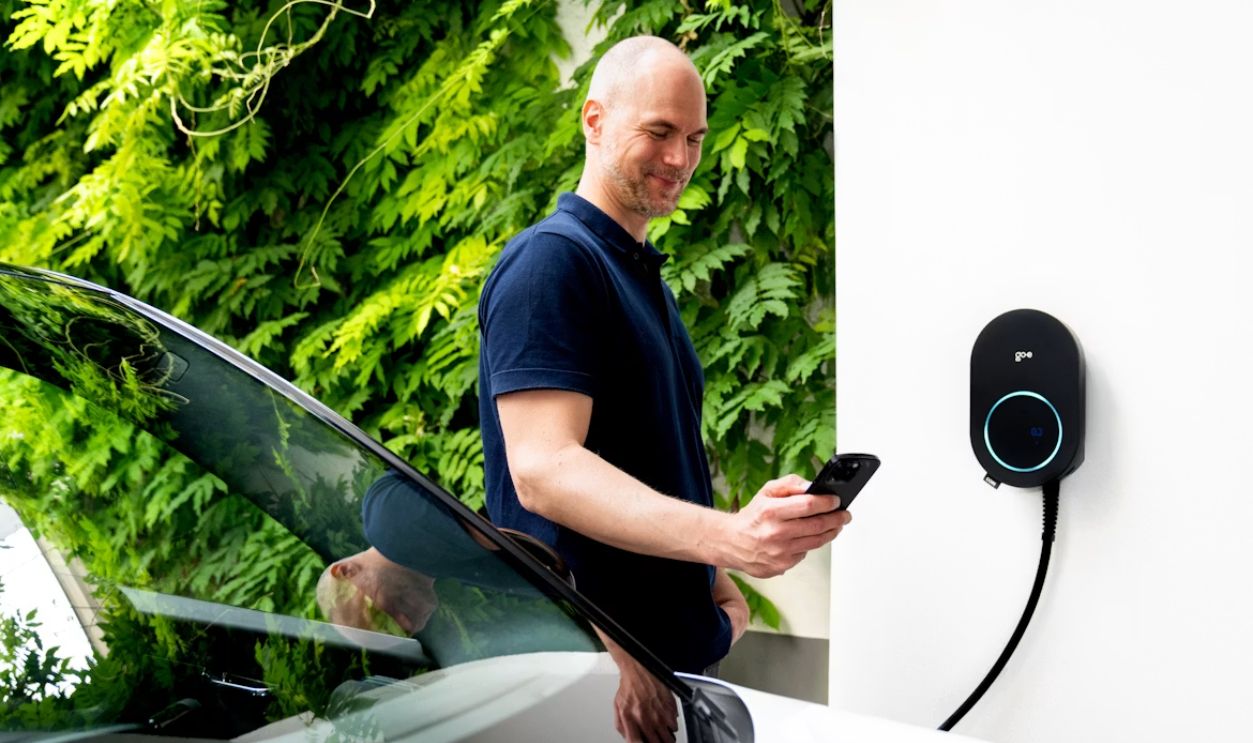 Man checks phone while charging his EV with the go-e Charger CORE