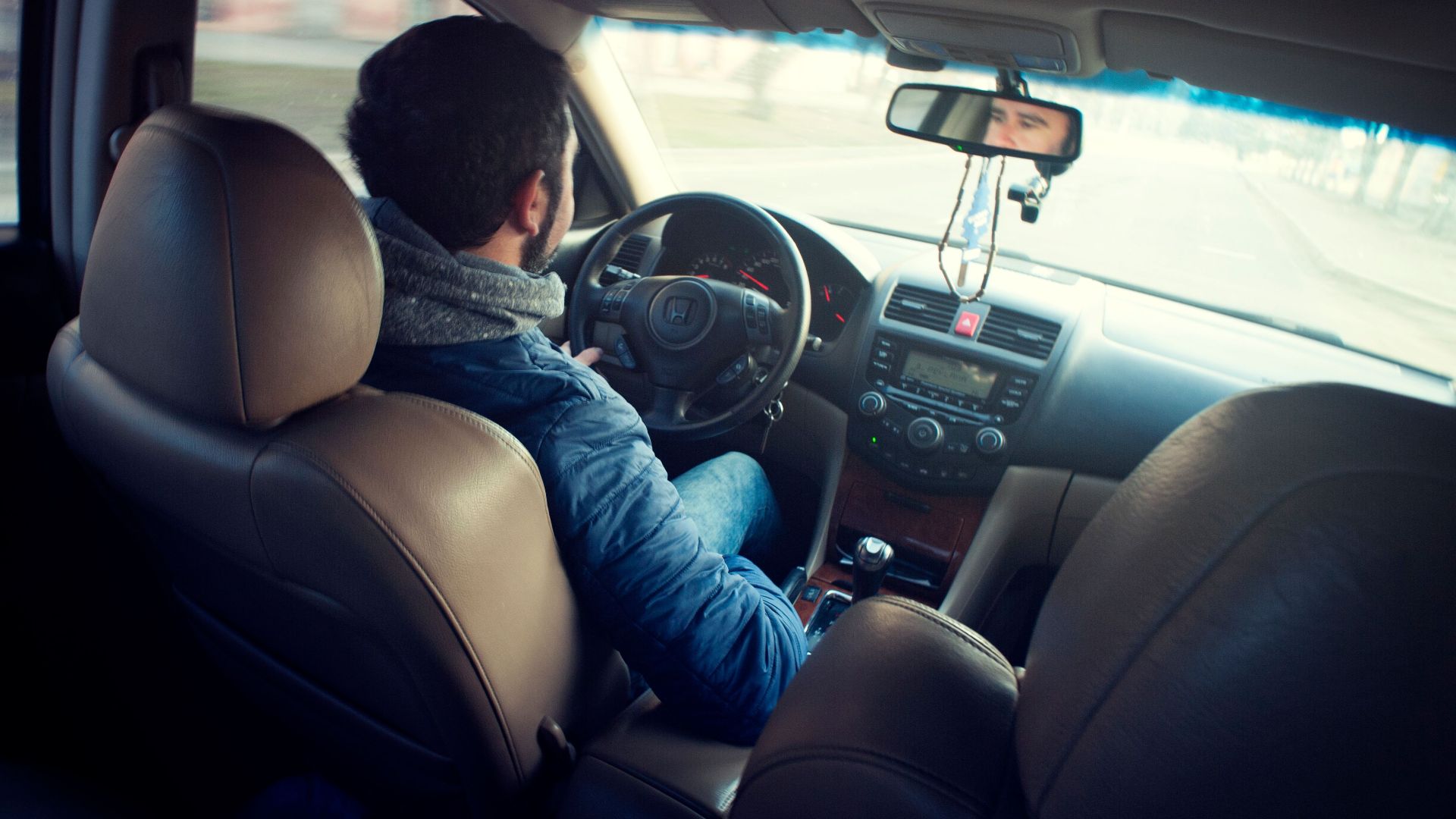 A man driving a car with focus on interior, dashboard, and steering wheel, captured from the backseat.