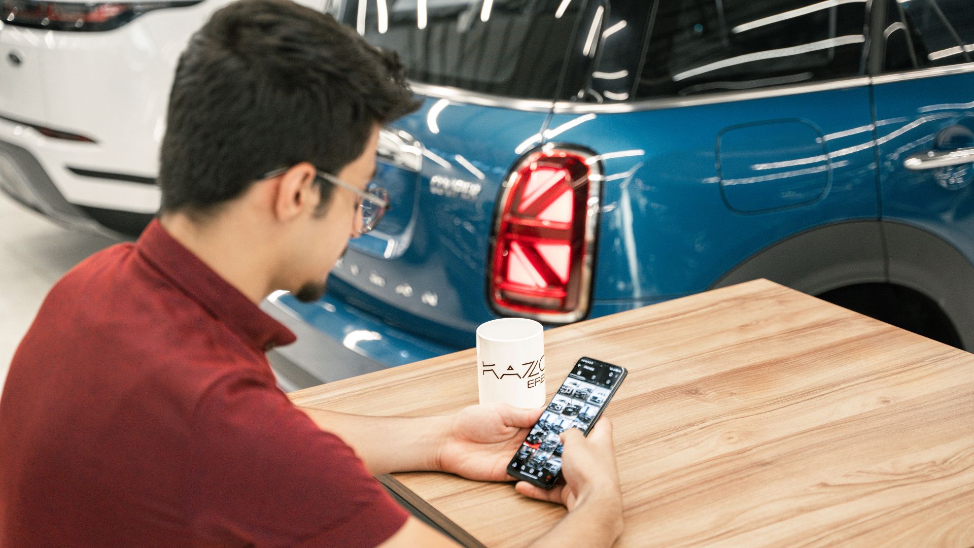 Young man at car dealership using smartphone. Modern cars in background.