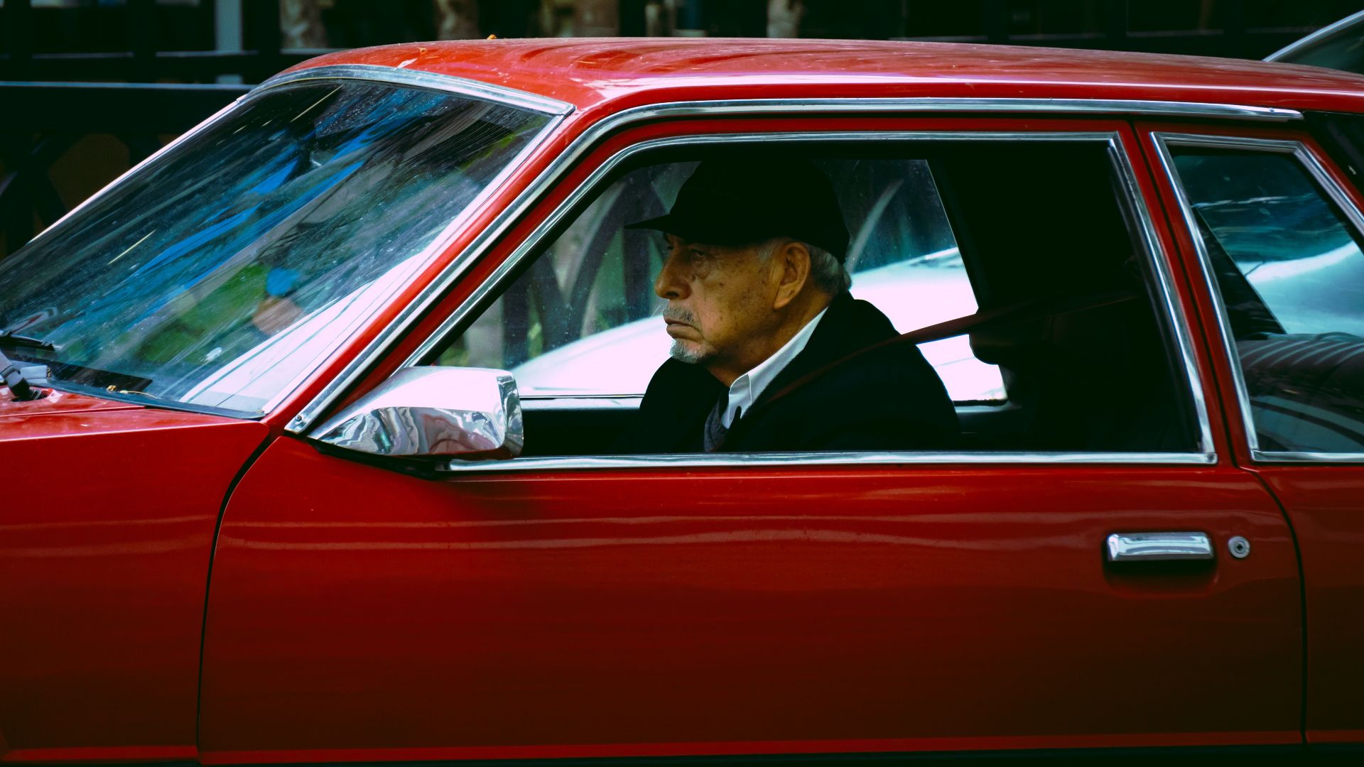 Elderly man driving a vintage red car through the streets of Callao, Lima.